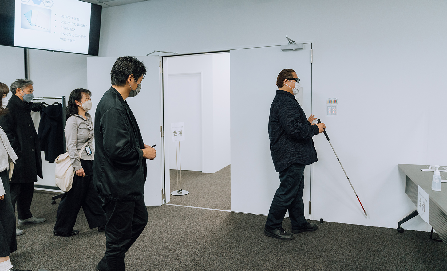 Empleados observando al usuario principal con un bastón blanco caminando en la sala de conferencias