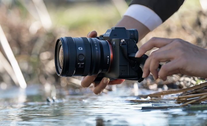 Un usuario sostiene una cámara α7 IV con un FE 16-25 mm F2.8 G cerca de la superficie de un río. Está capturando imágenes desde abajo.